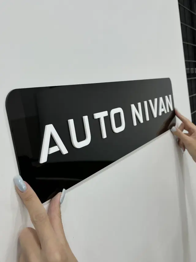 نمای نزدیک پلاک تبلیغاتی پلکسی مشکی با حروف سفید برجسته AUTO NIVAN در دست